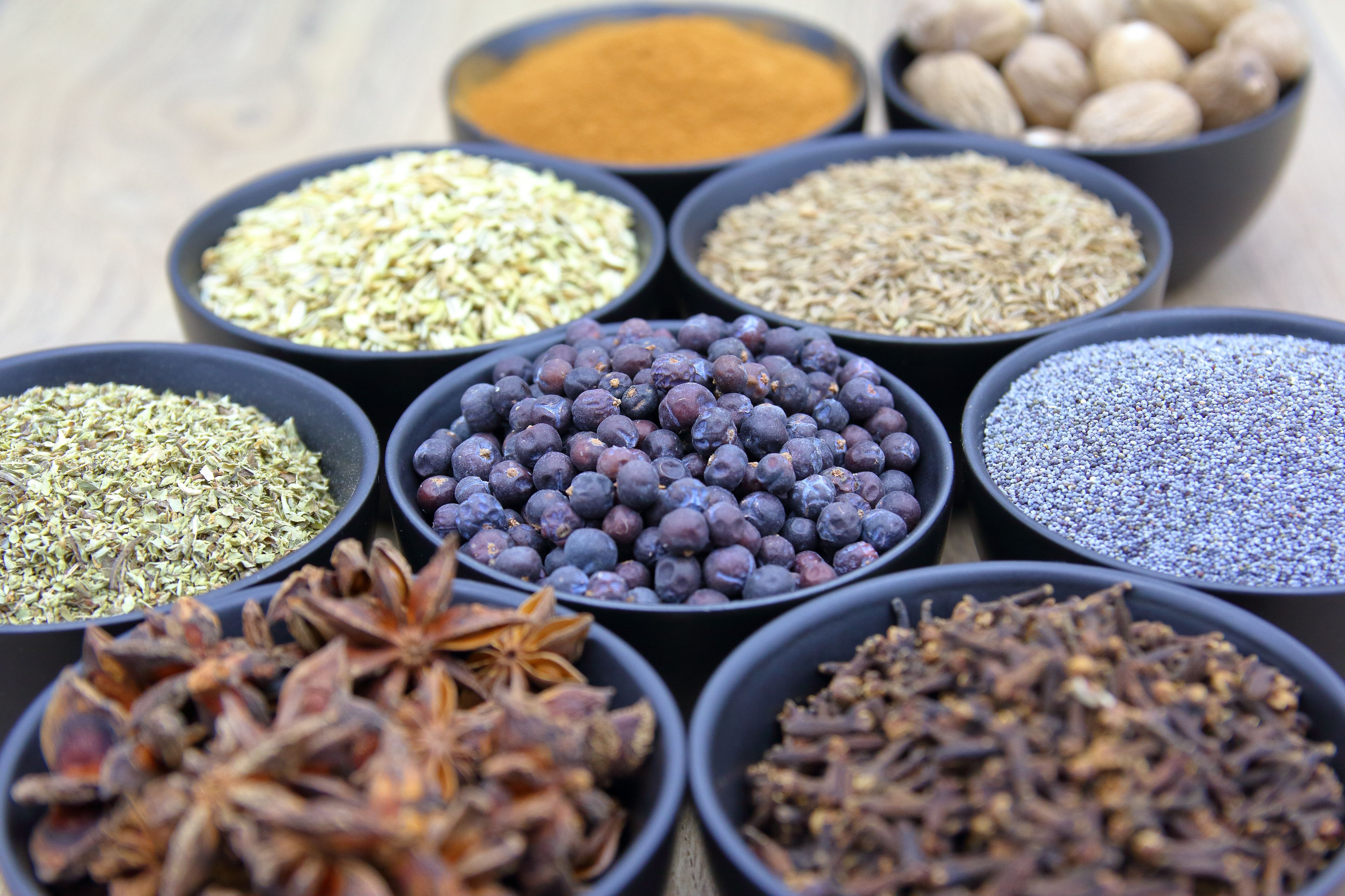 Assorted spices including star anise, cloves, and nutmeg in dark bowls